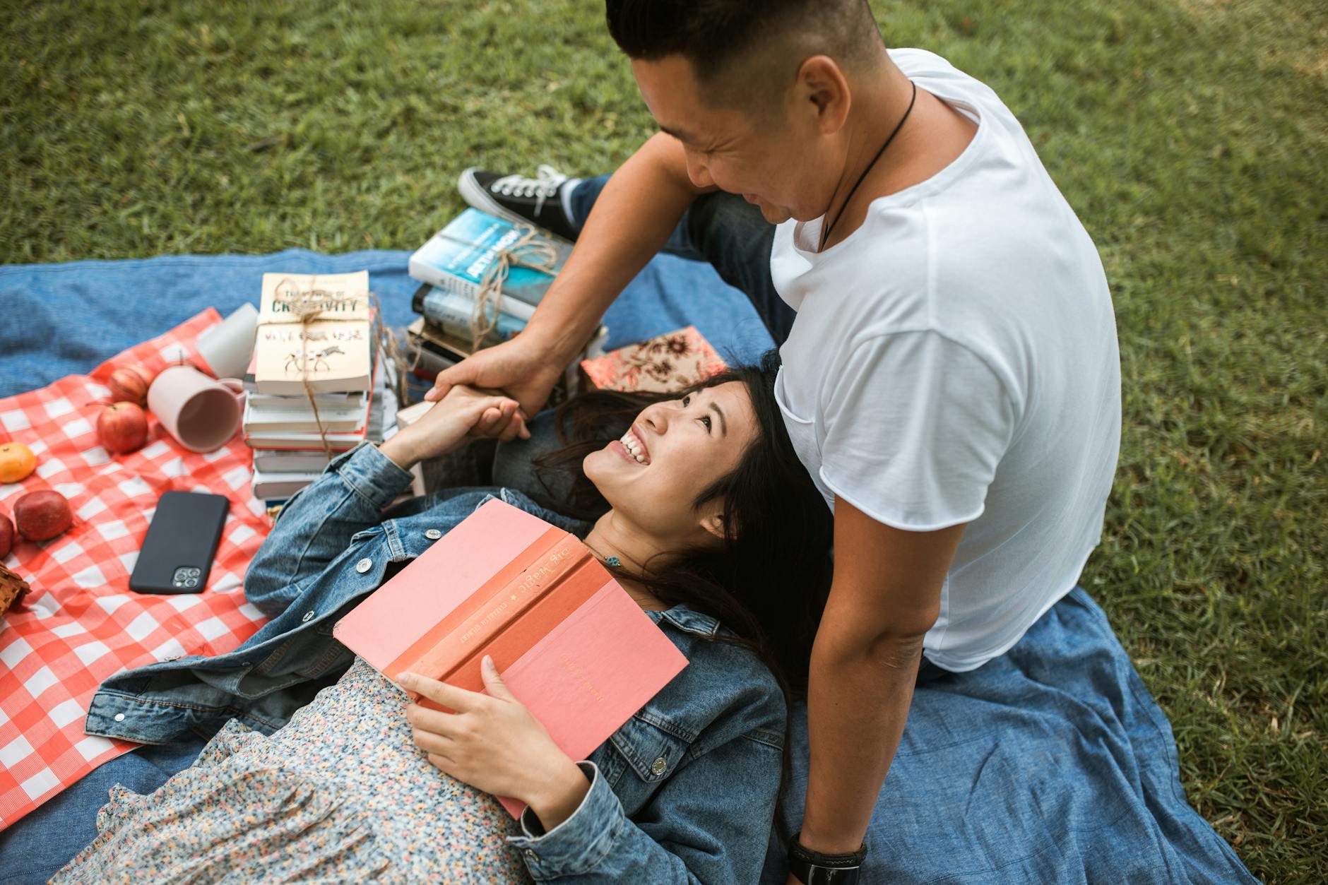 A matchmaker near me Asian couple sitting in a park with green grass smiling at each other