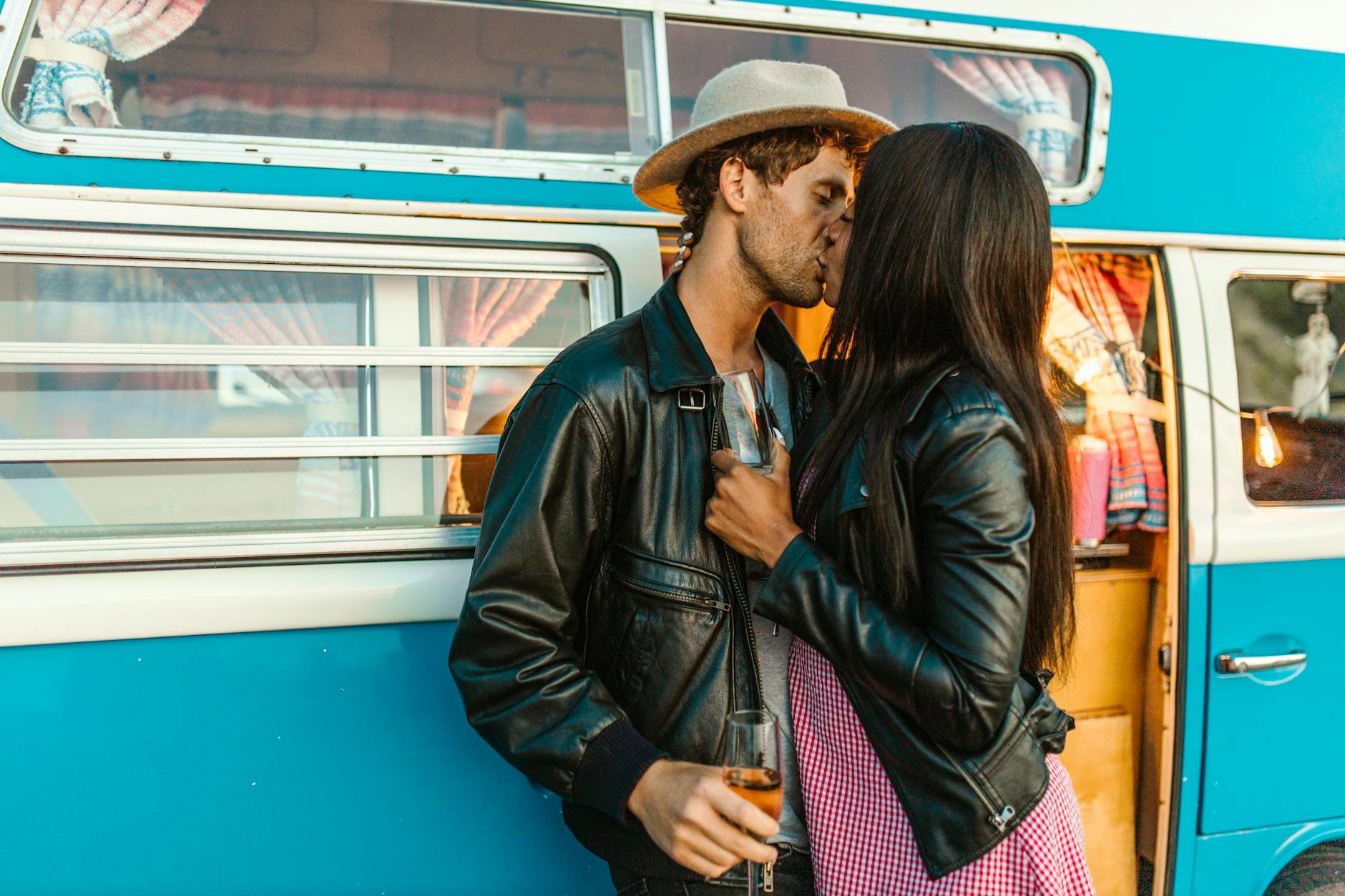 Interracial couple standing outside of a blue vintage mini van kissing